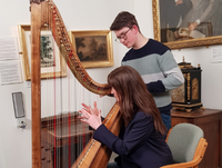 Image of award-winning harpist Gareth Swindail-Parry gives Bargain Hunt presenter Natasha Raskin-Sharp a lesson on how to play the Welsh Triple Harp at the Radnorshire Museum